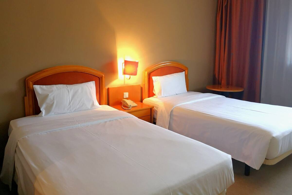A hotel room with two single beds, each with a wooden headboard, a bedside table with a lamp, and a telephone.