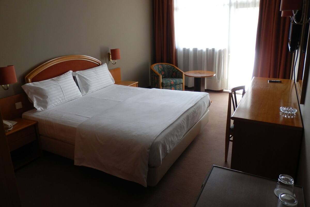 A hotel room with a large bed, a desk, a chair, a small table, and a TV.