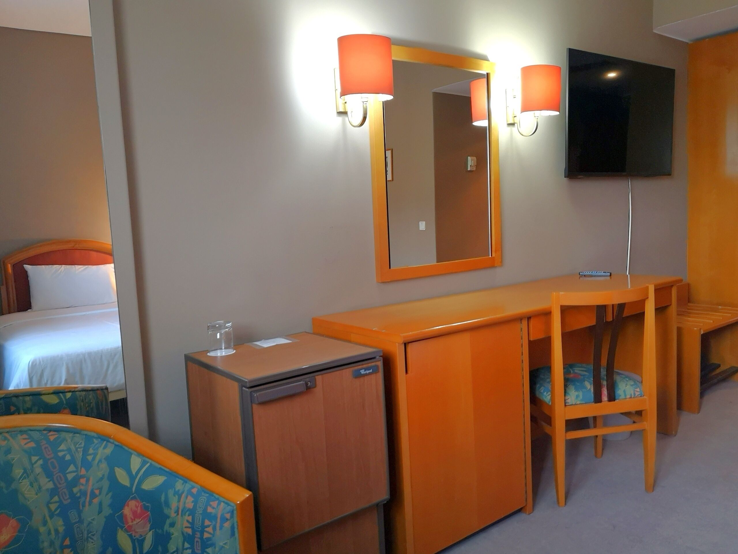 Een hotelkamer met een bed, een bureau, een stoel, een kleine koelkast en een televisie.