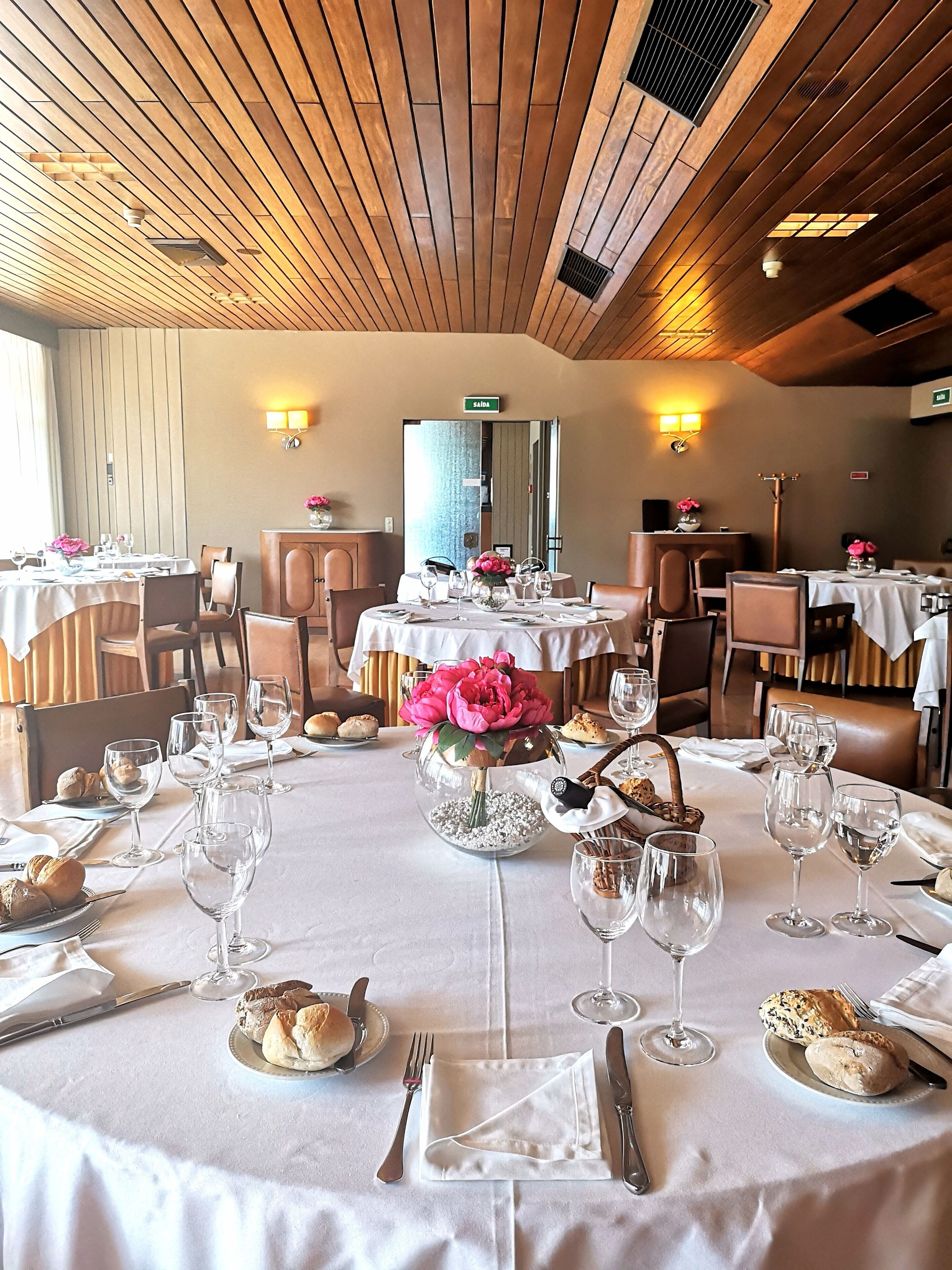 A restaurant with round tables set for dining, featuring white tablecloths, wine glasses, and floral centerpieces.