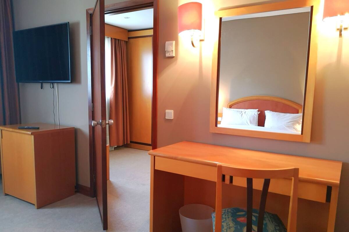 A hotel room with a desk, chair, and a large mirror.