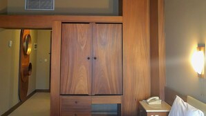 Ein Hotelzimmer mit Holzboden, einem großen Kleiderschrank, einem Nachttischchen mit Telefon und einem ordentlich bezogenen Bett.