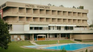Ein Hotel mit schlichter Fassade, mehreren Balkonen und einem Schwimmbad.