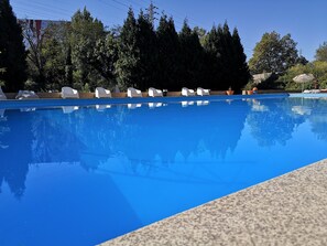A swimming pool with clear blue water, surrounded by trees and white lounge chairs. - Hotel Via Norte (Maia)