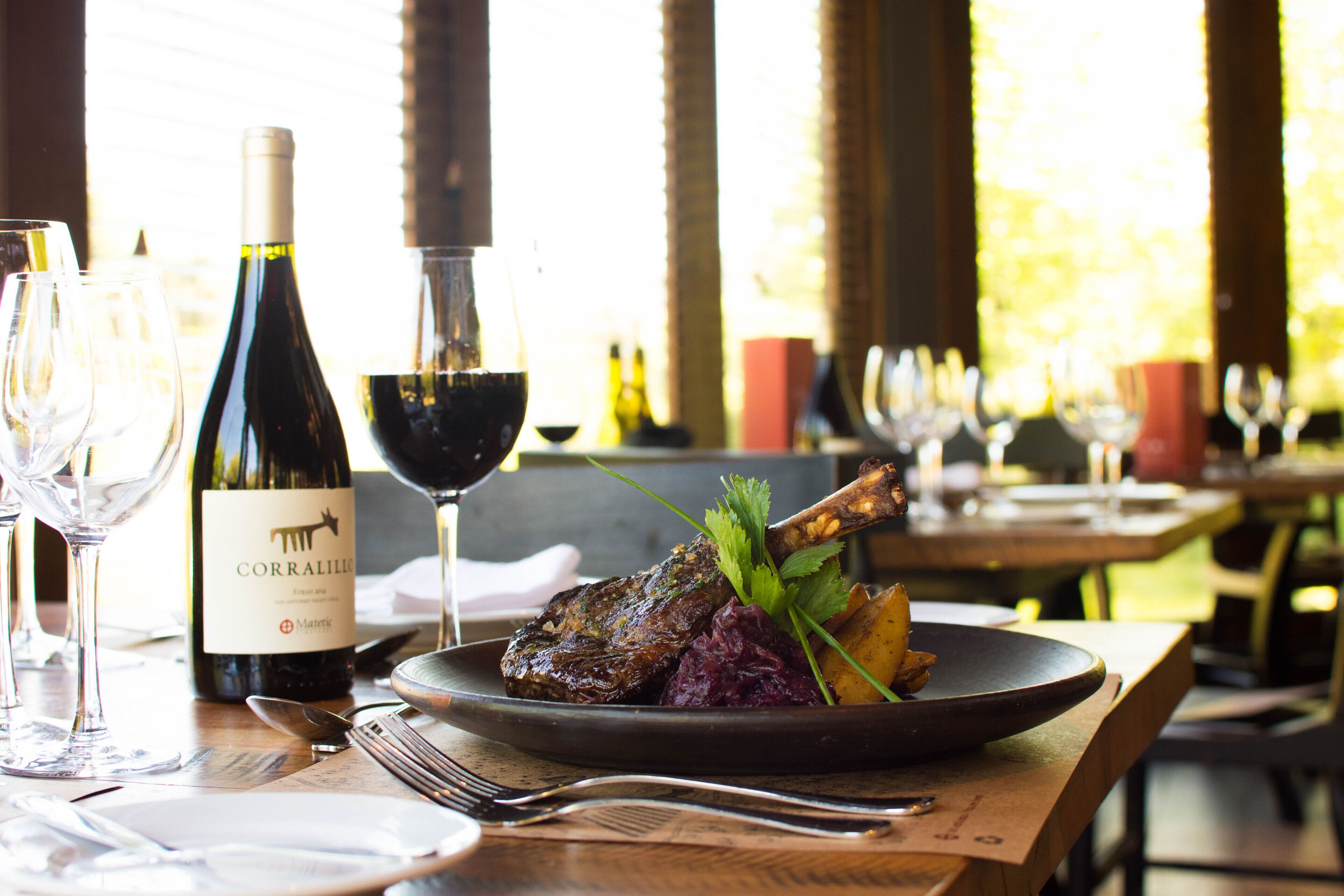 A dining table with a plate of food, a bottle of wine, and several glasses.