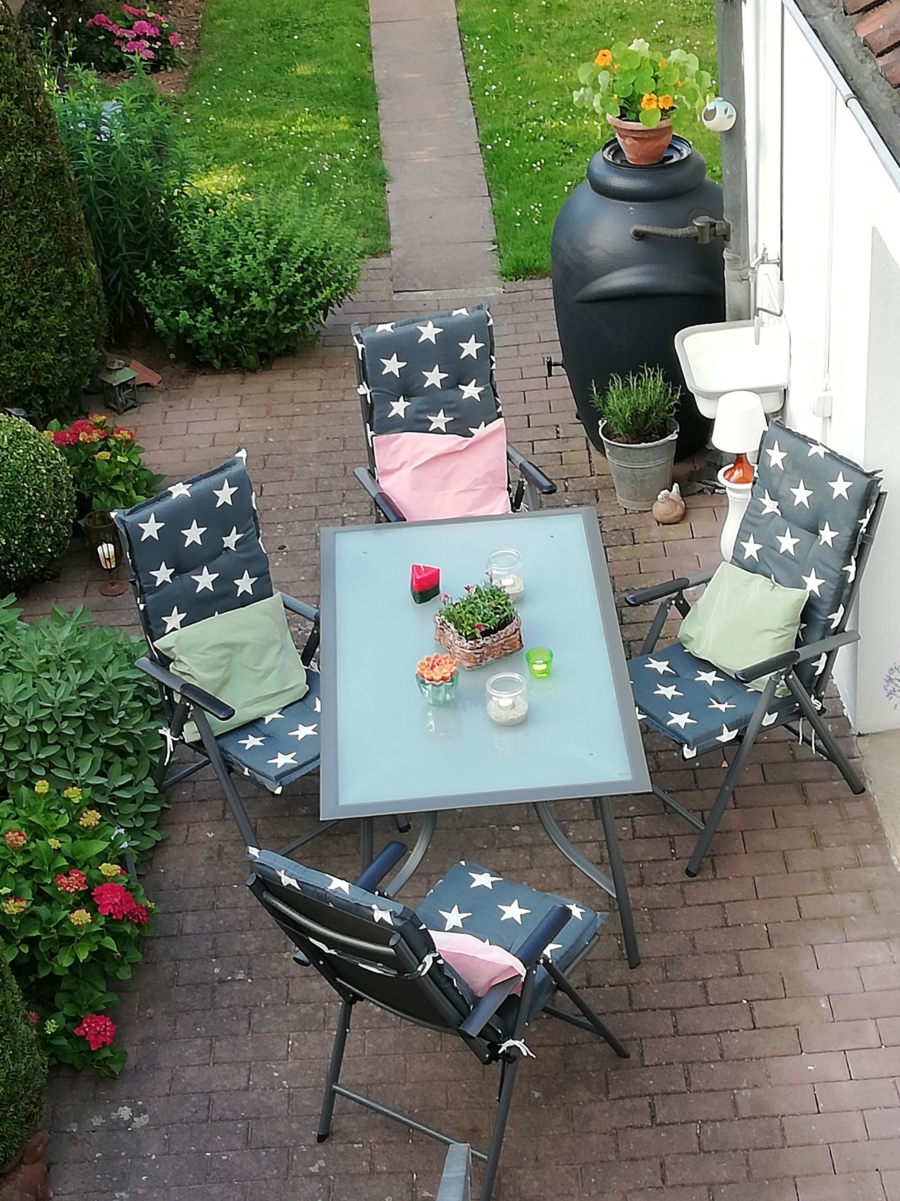 Une terrasse extérieure avec quatre chaises et une table, entourée de plantes et de fleurs en pot.