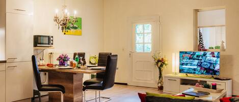A modern kitchen with a dining area, a living room with a sofa, and a TV displaying a movie.