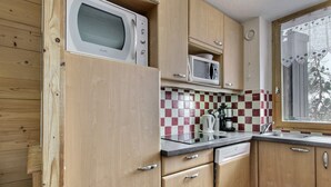 A compact kitchen with wooden cabinets, a microwave, a coffee maker, and a window with a view of trees.