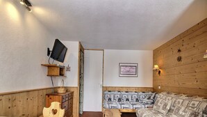 A cozy room with a wooden bed, a sofa, a wooden coffee table, a television on a shelf, and a door leading to another room.