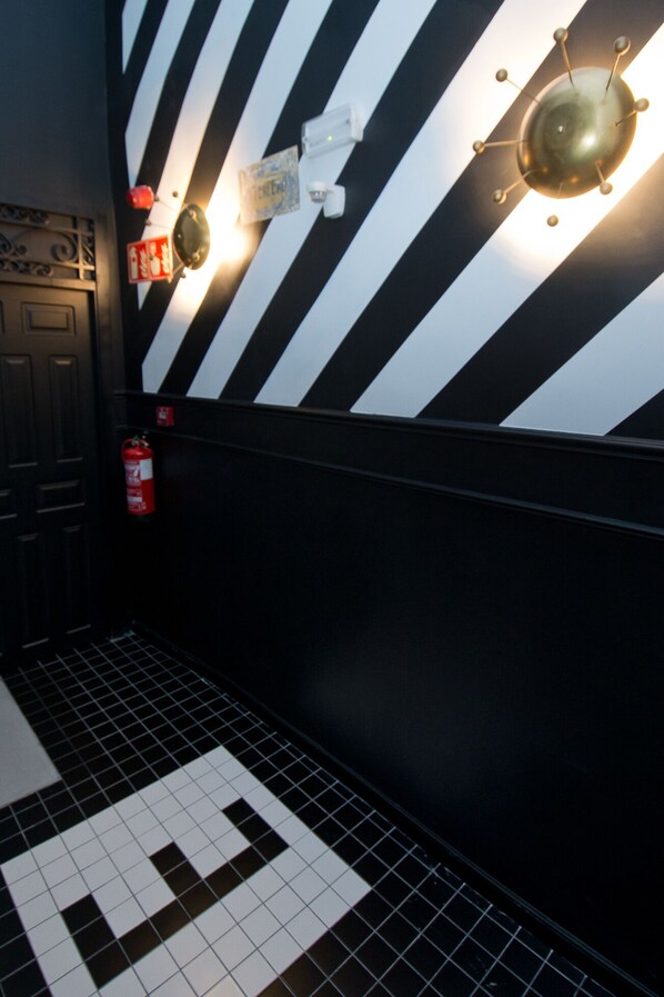 A hallway with black and white striped walls, a fire extinguisher, and a tiled floor. - Amor de Dios 17 Luxury Suites (Madrid)