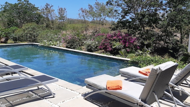 Una piscina rectangular con sillas de descanso y una sombrilla blanca.