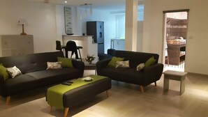 Una sala moderna con dos sofás negros, un otoman verde y una mesita.