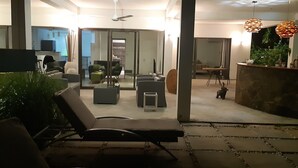 Una sala moderna con sofá, sillones y una mesita de centro. Cuenta con un comedor con sillas y una mesa. La habitación tiene un ventanal grande y un ventilador de techo.