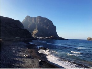 A coastal landscape with a rocky beach, a large cliff, and calm sea. - Jaca - Hostel (Machico)