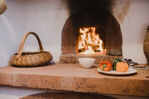 A brick oven with a fire, a plate with bell peppers, a bowl, and a wicker basket. - Jaca - Hostel (Machico)