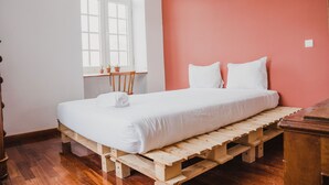 A room with a bed on a wooden pallet, a window with potted plants, and a red wall. - Jaca - Hostel (Machico)