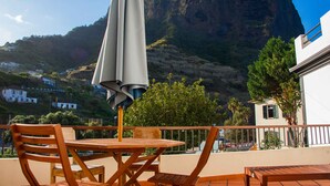 A terrace with a table and chairs, a large umbrella, and a view of a mountain and houses. - Jaca - Hostel (Machico)