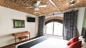 Un dormitorio con una cama grande, un escritorio, un televisor y una ventana con cortinas.