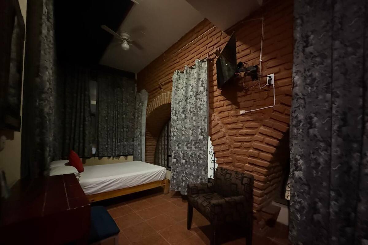 Een slaapkamer met een bed, een stoel, een klein tafeltje en een bakstenen muur.