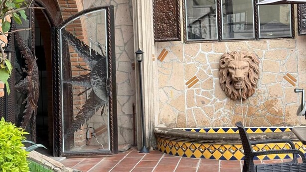 Un patio al aire libre con un muro de piedra, una decoración con cabeza de león y suelo de baldosas.