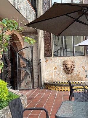 An outdoor patio area with a stone wall, a lion head decoration, and a tiled floor. - Hotel Hacienda Tonalmain, Central Nueva (Tonalá)