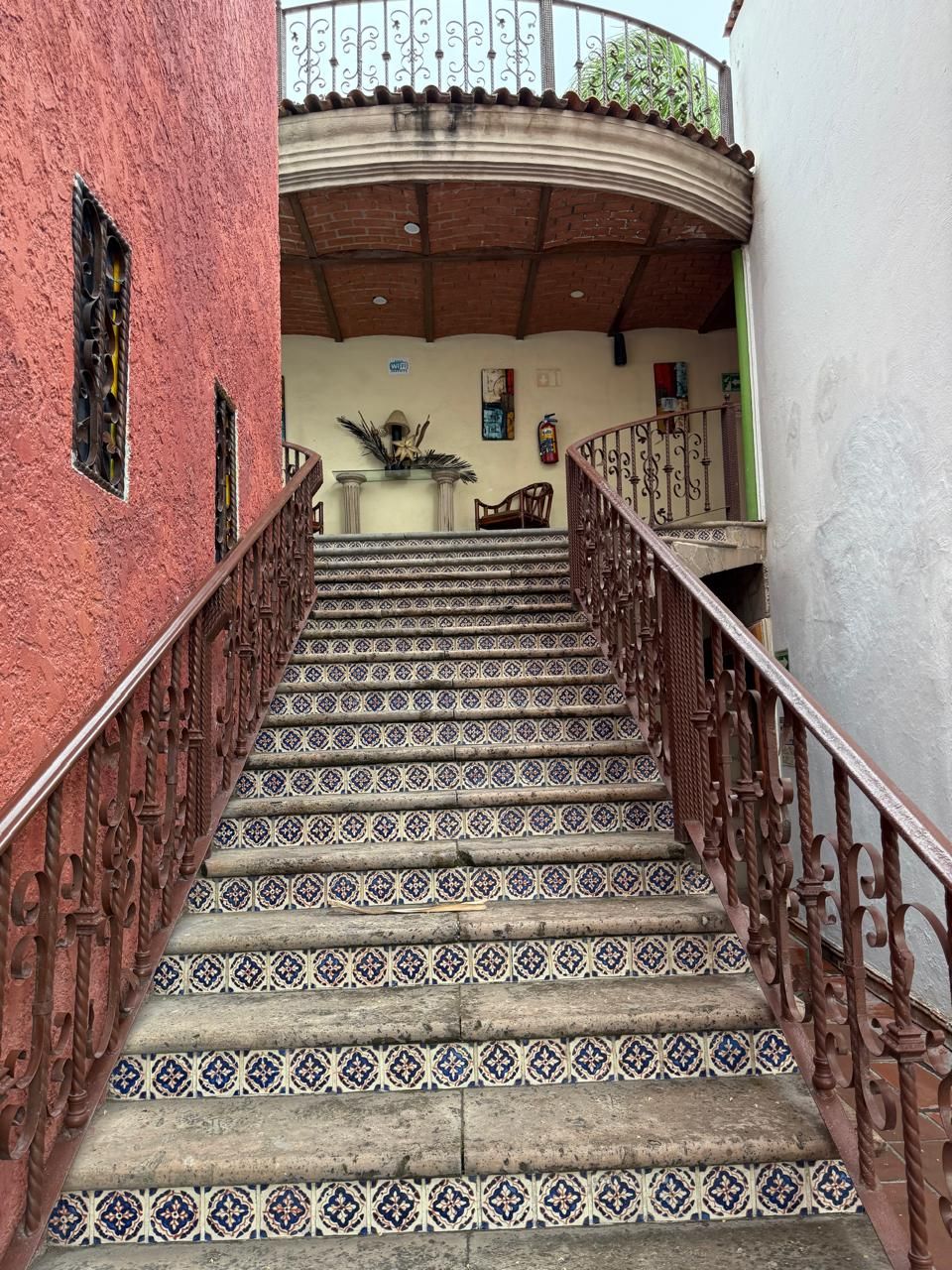 Una escalera con baldosas estampadas y barandillas de hierro forjado que lleva a un balcón.