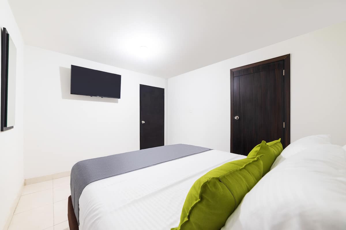 A bedroom with a bed, a flat-screen TV mounted on the wall, and a dark wooden wardrobe.