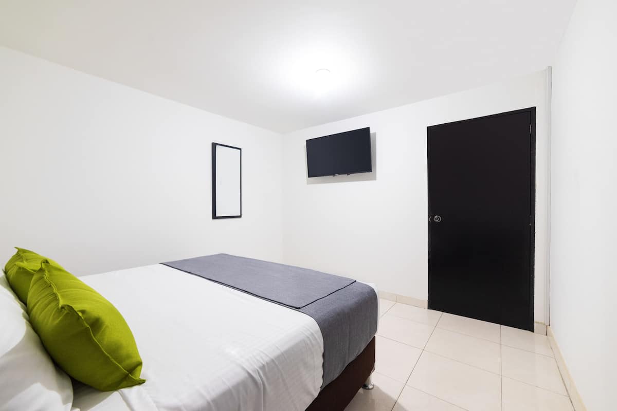 A bedroom with a bed, a TV mounted on the wall, and a door.