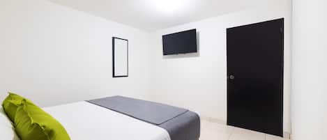 Un dormitorio con una cama, un televisor montado en la pared y una puerta.