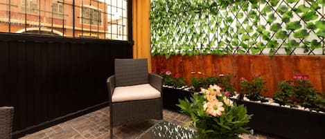 Un patio con una silla de mimbre, una mesa de vidrio y plantas en macetas.