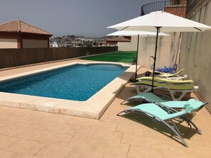 Una piscina al aire libre, sombrillas, sillones reclinables de piscina