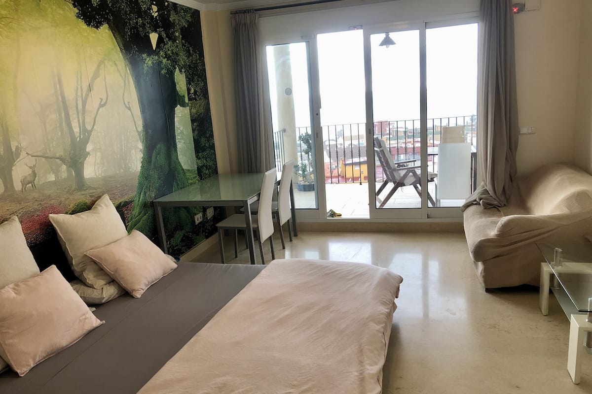 Ett modernt hotellrum med en stor säng, ett matbord och en balkong med utsikt över staden.