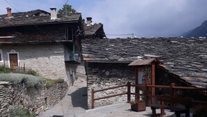Une rue pavée bordée de bâtiments en pierre, un banc en bois et une petite structure en bois avec une enseigne.