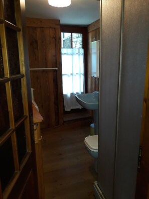 A wooden-paneled bathroom with a toilet, sink, and a window with a view of a fence. - Cabin in characteristic mountain village (Bellino CN)