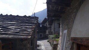 Une ruelle étroite pavée, bordée de bâtiments traditionnels en pierre, dotés de portes et de fenêtres en bois.