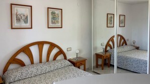 A bedroom with a wooden bed, a bedside table with a lamp, and two framed pictures on the wall.