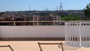 A rooftop terrace with a view of a cityscape, including buildings and amusement park rides.
