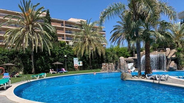 A swimming pool with lounge chairs, palm trees, and a waterfall feature.