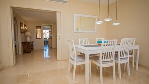 A dining area with a white table and chairs, a mirror on the wall, and pendant lights.