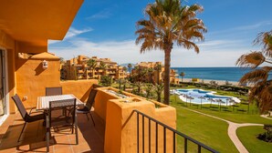 A balcony with a table and chairs, overlooking a pool and beach.