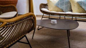 Una silla de mimbre, una mesa redonda con un objeto encima y un sofá con cojines estampados.