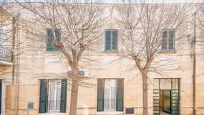 Un edificio con una entrada amplia, dos árboles delante y una ventana con contraventanas.