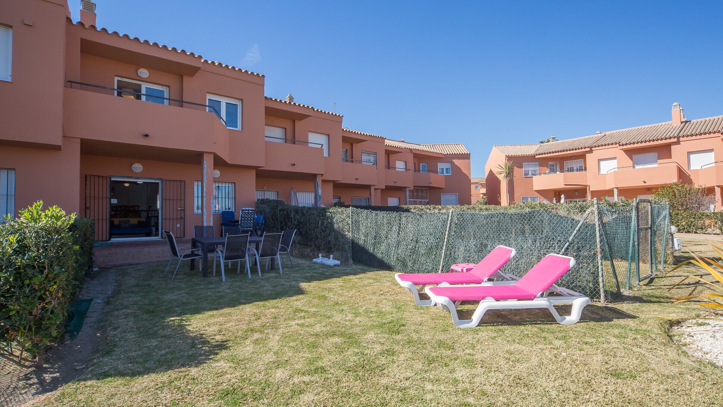 Un patio con mesa de billar, sillas y tumbonas rosadas.