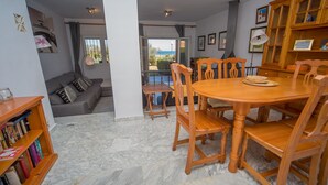 Un coin repas comprenant une table et des chaises en bois, une petite table d’appoint et un canapé avec des coussins.