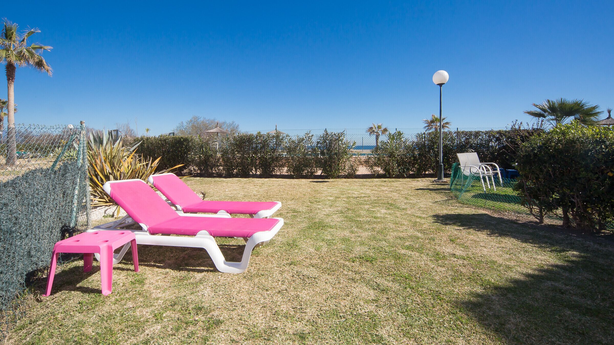 A grassy outdoor area with two pink lounge chairs and a small table.