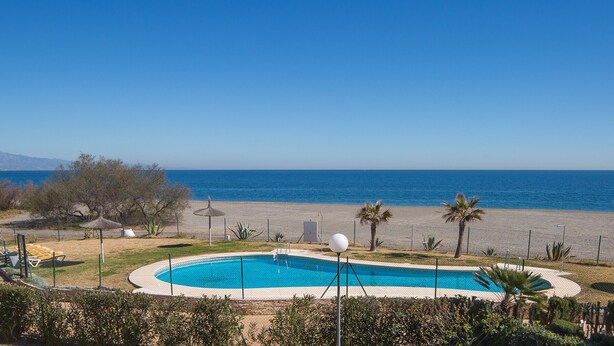 Une piscine avec vue sur la mer, entourée de palmiers et délimitée par une clôture.