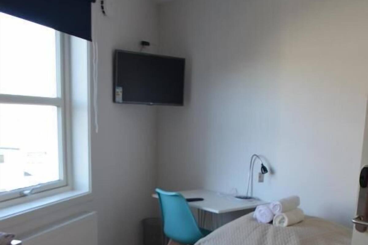 Un dormitorio pequeño y moderno con una cama, un escritorio, una silla y un televisor.