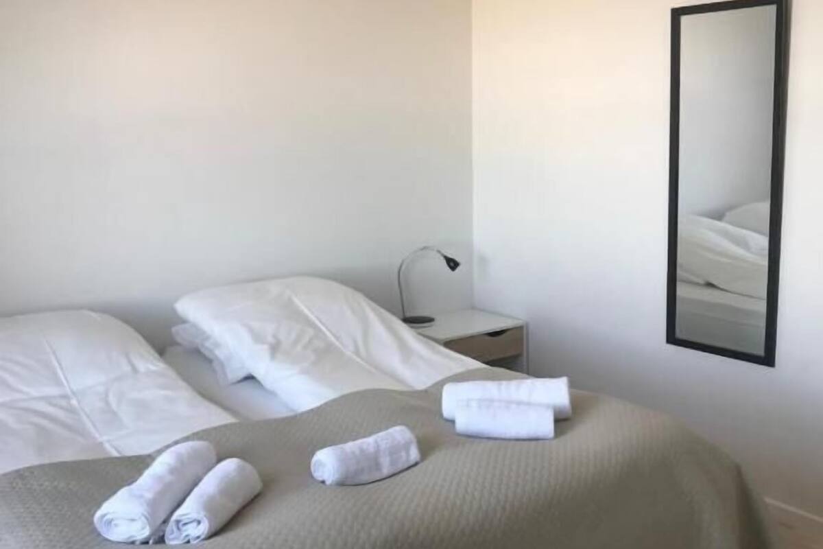 Una habitación de hotel con una cama, dos almohadas, una mesita de noche, una lámpara y un espejo en la pared.