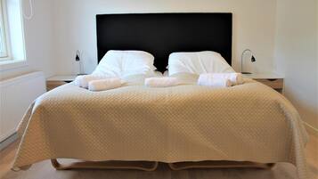 Una cama bien hecha con un edredón acolchado, dos almohadas y dos toallas enrolladas sobre las mesitas de noche.
