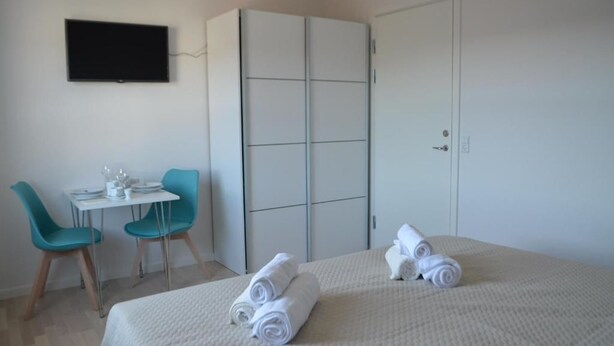 A hotel room with a bed, two chairs, a small table, a TV, and a wardrobe. - Hotel Nuka (Ilulissat)